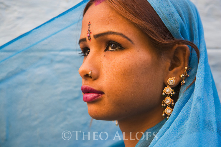 Rajasthani girl in blue dress and traditional Rajasthani jewelry in front of blue house wall in Jaisalmer Fort